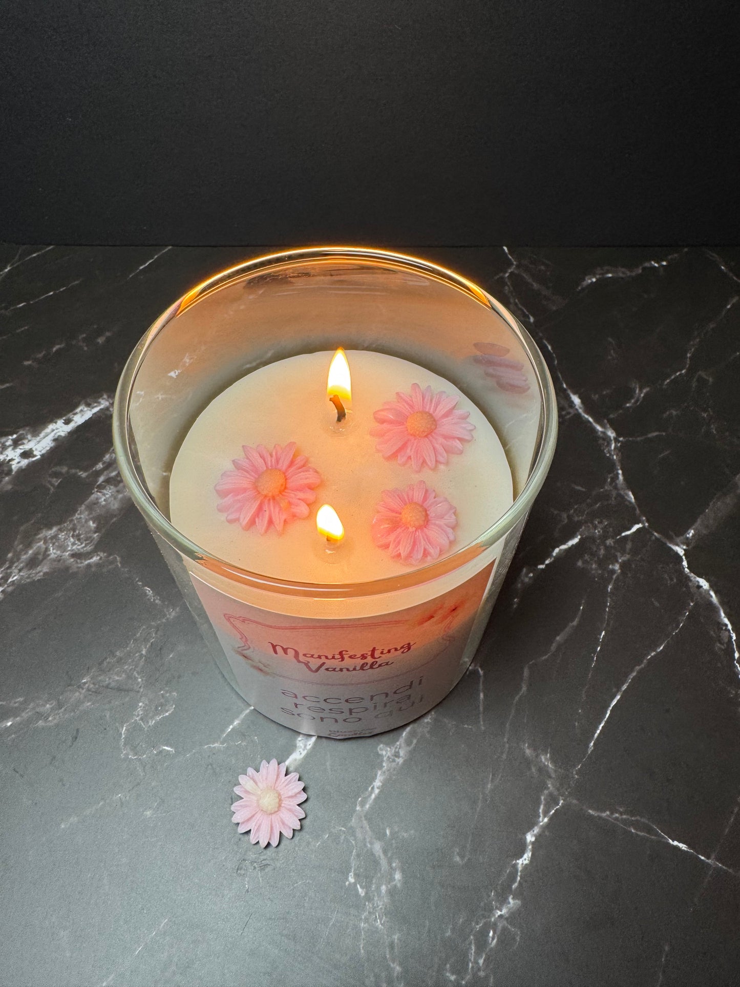 candela in vetro accesa con tre fiorellini rosa sopra