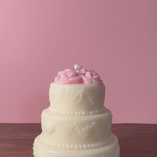 candela a forma di torta a tre piani decorativa con fiori sulla parte superiore e decorazioni sui lati